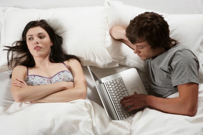 Young man and woman lying in bed, man using laptop, overhead view